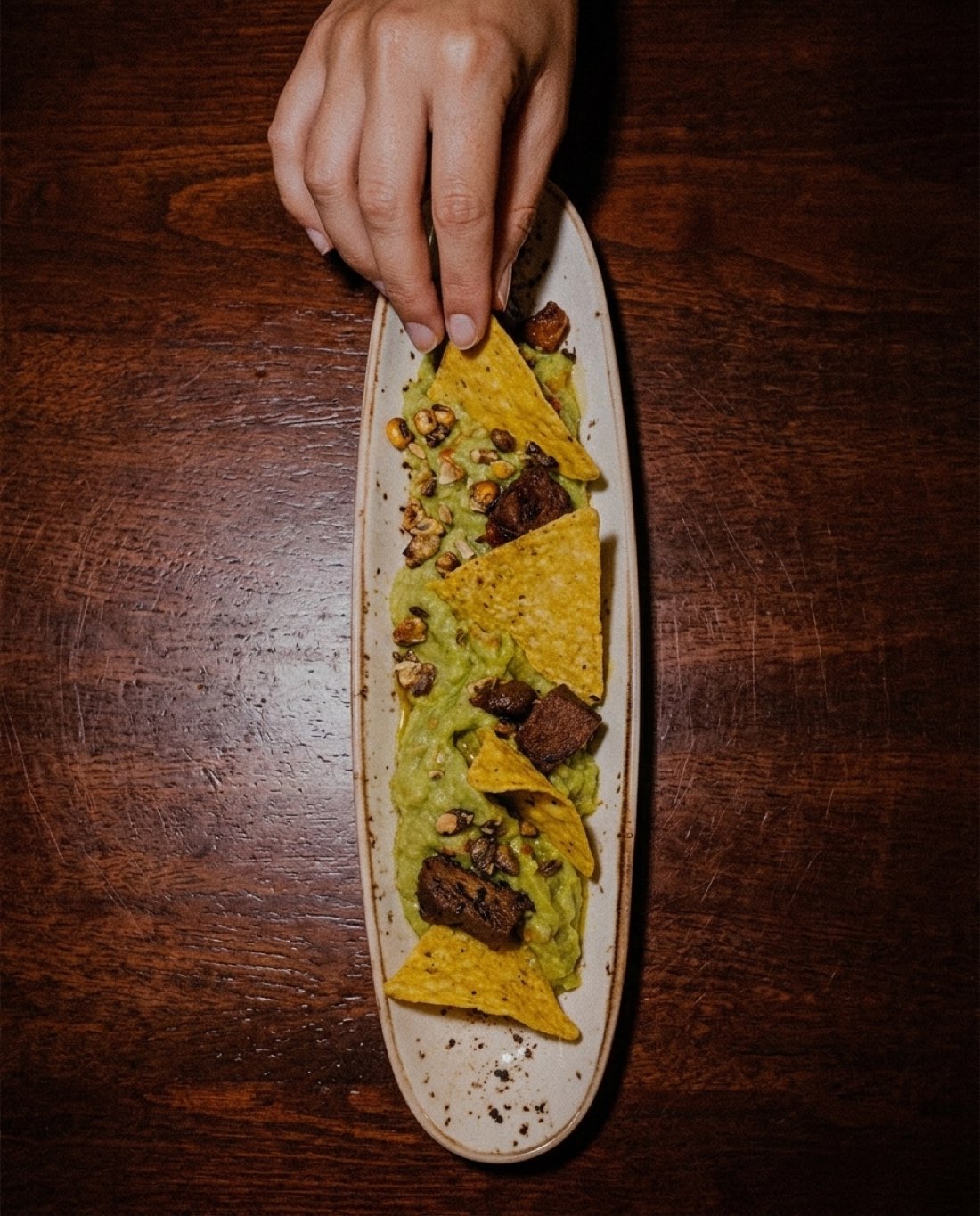 Guacamole casero con chicharrón de atún, pipas garrapiñadas y nachos, en plato alargado