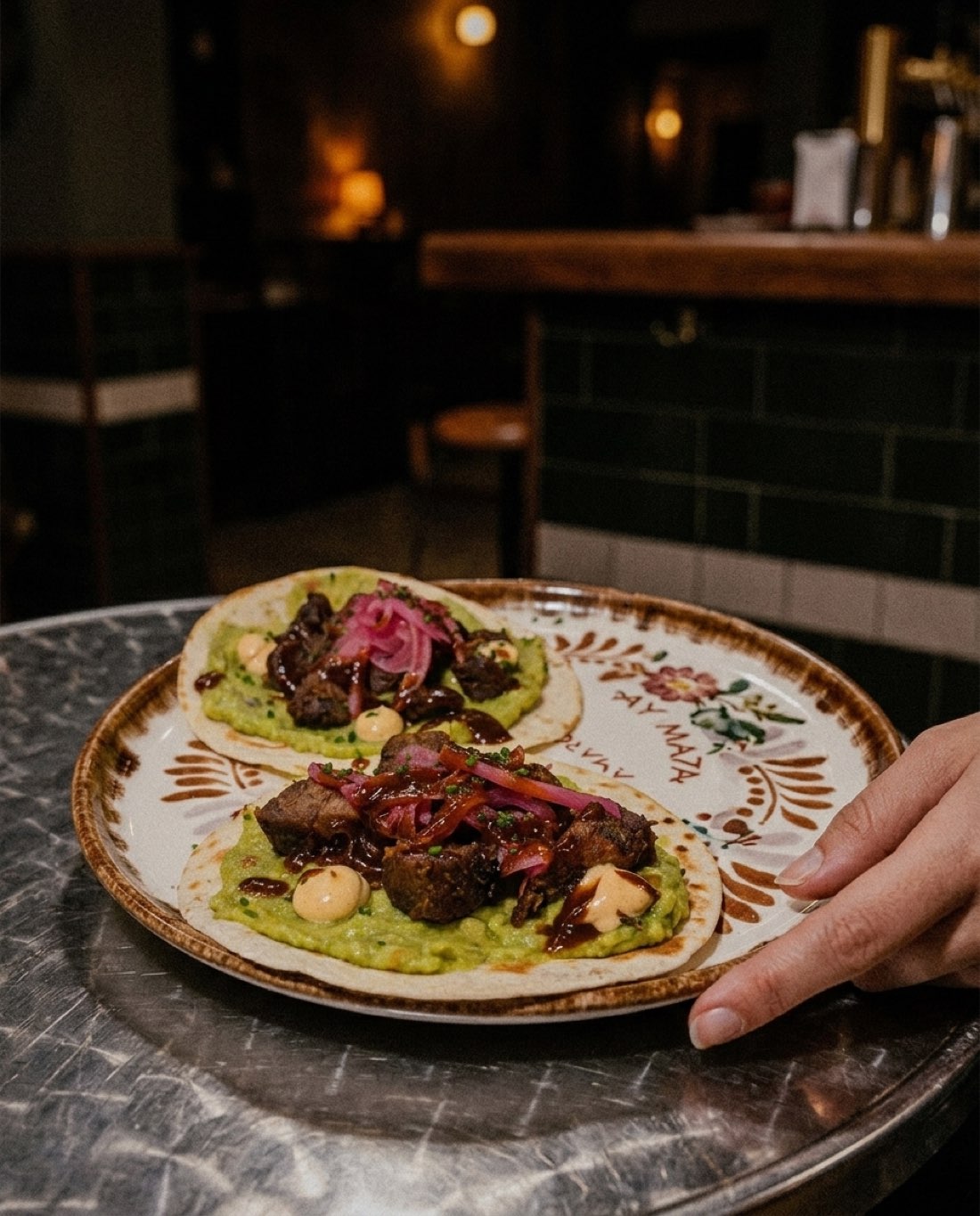 Dos tacos de chicharrón de atún con guacamole y cebolla encurtida, en plato de cerámica sobre la mesa